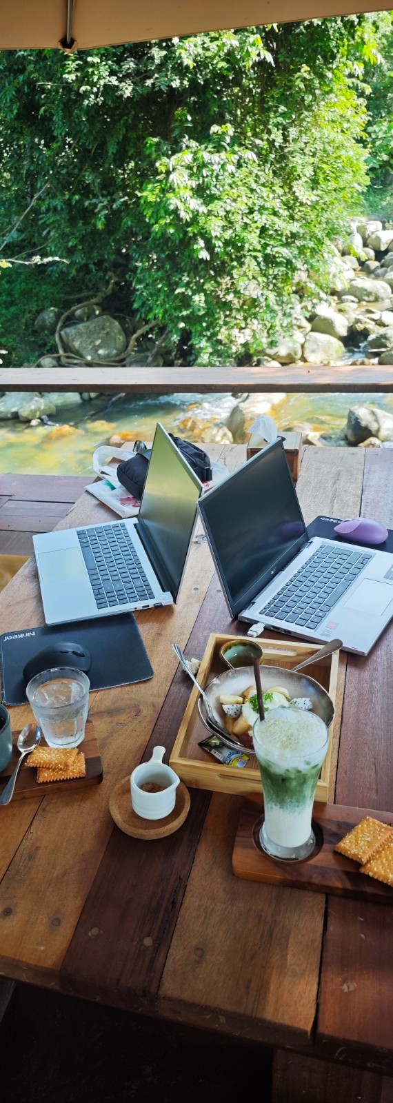Deux ordinateurs portables sur une table en bois, face à une rivière dans la jungle